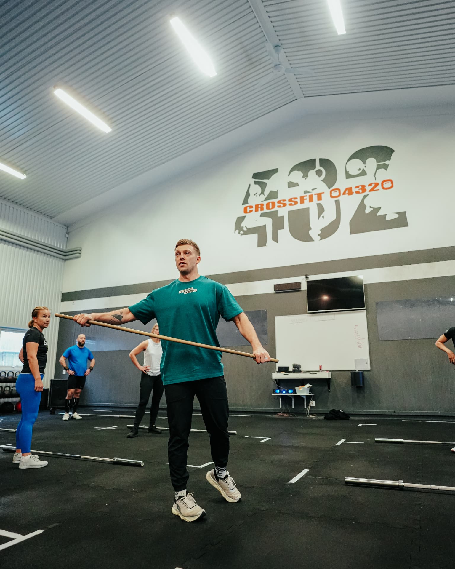 Coach in a Prepared shirt leading a class with PVC pipes in a CrossFit gym