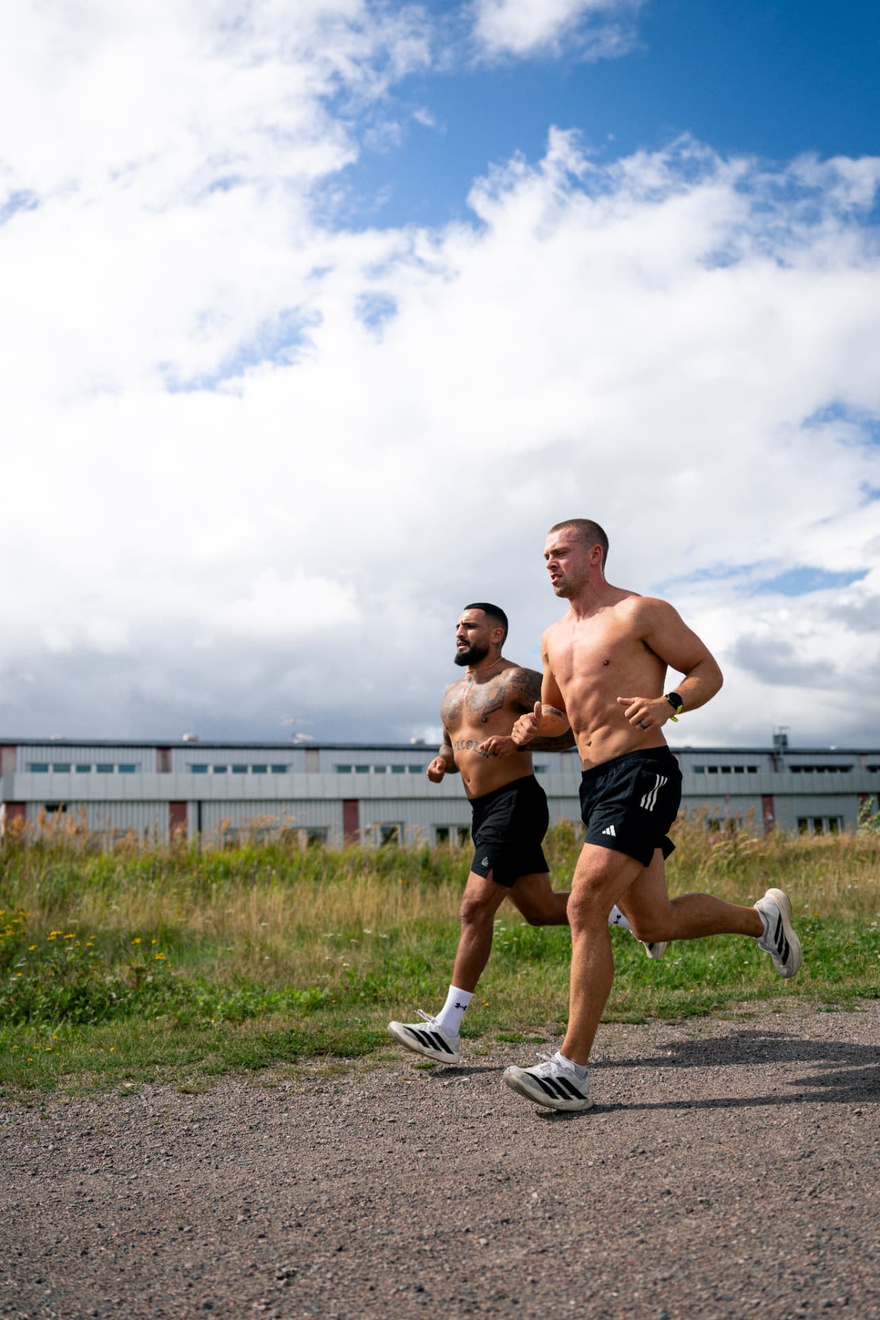 Two athletes running side by side on a gravel path under a bright sky