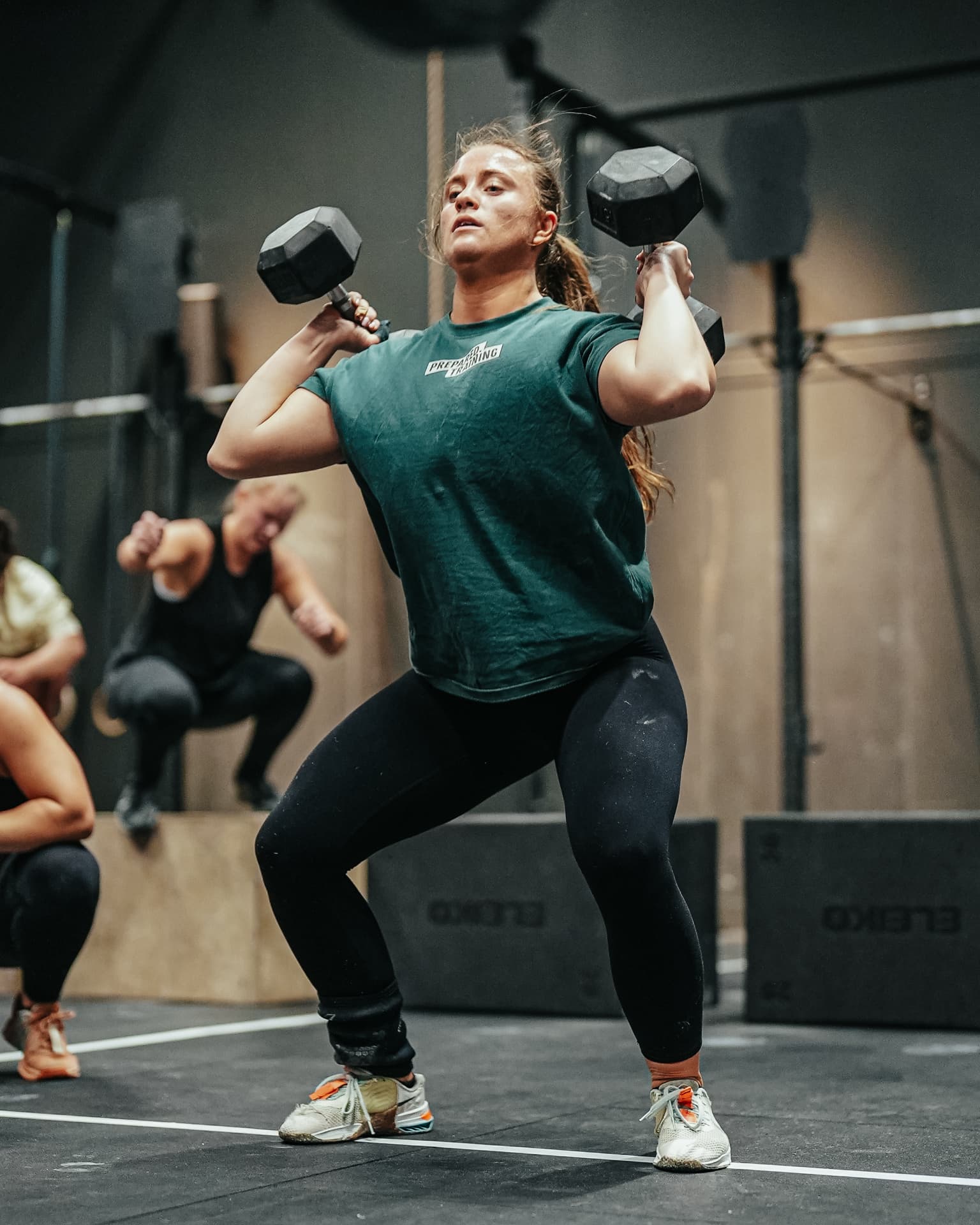 Athlete pressing dumbbells overhead in a Prepared training tee